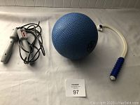 Photo of the lot showing a gray plastic handle jump rope with cord, a blue textured exercise ball, and a white plastic handle back massager with blue knobs on a white surface.