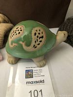 Green ceramic turtle figurine placed on a white surface with a brown background