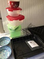 Photo showing stacked plastic containers with red and green lids, decorative bowls, and turkey roaster rack.