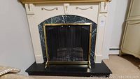 Front view of electric fireplace showing mantel, marble-look surround, brass mesh screen and log set