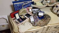 Wide photo showing assorted costume jewelry on tray and vanity including necklaces, earrings, pins, watch, beaded bag, wallet, scarves, and jewelry organizer.