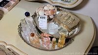 Photo showing two mirrored trays holding generic scent bottles, lotion bottle, shell-encrusted keepsake box, clear glass heart-shaped dish, and ornate footed metal box with embossed figures.