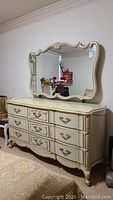 French provincial style long dresser with nine drawers and metal handles, scalloped front and scroll legs, cream painted with gold accents.