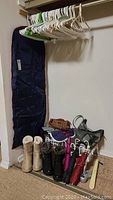 Photo of garment bag hanging on wall, plastic and metal shoe racks holding boots, purses, and umbrellas, and assorted clothing hangers on a rack.