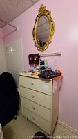 Photo of the four drawer dresser with various items on top and gold-toned oval mirror hanging above, showing overall lot contents.