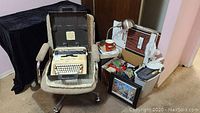 Full view of the upholstered office chair with the Olivetti Lettera 35 typewriter in its carrying case placed on the chair seat, surrounded by other items including framed picture, shredder, fans, and boxes.
