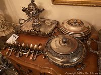 Two large round silver plated covered dishes with enamelled inserts, decorative handles; silver plated sugar bowl with tea spoon holder and 6 spoons; wall mounted spoon holder with 8 travel spoons; etched serving tray with handles, tarnished.