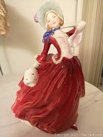 Front side view of Royal Doulton Autumn Breezes figurine showing detailed facial features, bonnet with purple tip, and flowing red dress.