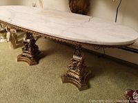 Full view of oval white marble top and gilt metal base with cherubs