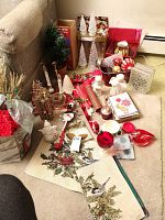 Overview of assorted Christmas decorations including candle holders, taper candles, cards, placemats, wreath hanger, planter, ornaments, glass vase, and gift bags arranged on carpet and sofa.