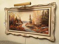 Front view of the framed landscape painting with attached picture light