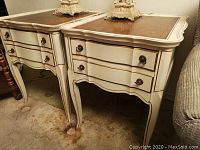 Pair of painted wood end tables with curved legs, brass drawer pulls, and leather-like textured brown tops.