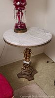 Full view of the round table showing the white marble top, metal base, and gold cherubs.