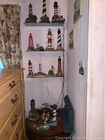 Overview of lighthouse figurines displayed on three shelves and a small wooden table, with varying heights and colors including striped and solid patterns.