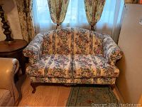 Front view of floral upholstered loveseat showing pattern, shape, and wooden legs.