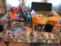 Full assortment of Halloween decorations on floral sofa including quilt, disco ball, pumpkin lights, and storage bin with additional Halloween items