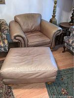 Full view of the brown leather chair and matching ottoman showing overall shape and nailhead details.