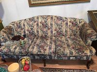 Full front view of the floral patterned upholstered sofa with curved back and visible wooden legs