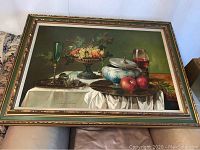Front view of still life painting showing fruit bowl, glassware and tureen in gold-accented frame