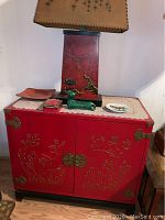 Front view of Asian red wooden chest with floral embossed brass hardware, showing top decoration including lamp and small decor items.