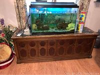 Front view of the wooden cabinet with a fish tank placed on top. Cabinet has carved circular patterns on front panels and dark wood finish.