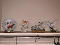 Overview of all four items: Jonathan Byron plate, Seraphim Classics angel figurine, Royal Crown swan music box, and Masterpiece porcelain doves, displayed on a shelf.