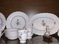 Full display of the dinnerware set including plates, cups, creamer, sugar bowl, serving platter, owl figurine and cut glass dinner bell on a wood shelf.