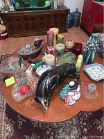 Photo showing various ceramic and glass items including black ceramic bull, candles, and small decorative pieces on a wooden table.
