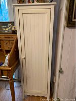Full front view of tall white wooden pantry cabinet with closed door, showing vertical groove design and round wooden knob.