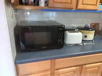 Sharp black microwave, Hamilton Beach toaster oven, Rival crockpot, white toaster on kitchen counter