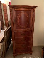 Front view of closed lingerie chest showing overall design, curved drawers, door panel and brass handles