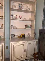 Mazor bookshelf hutch with multiple shelves displaying various small decor items and figurines, lower cabinet with closed doors, painted in cream color
