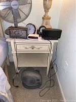 Left nightstand with digital alarm clocks and fan on top, showing overall condition.
