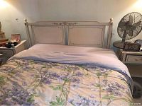 Front view of the bedframe with headboard and footboard, dressed with linens including a floral comforter and light blue blanket