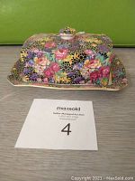 Rectangular Royal Winton butter dish with floral roses pattern and gold trim, with lid on plate in front of green background.