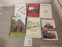 Six vintage cookbooks displayed on a plain surface, showing varied designs and titles.