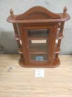 Front view of the wooden wall curio cabinet showing glass door, side shelves, and decorative top.