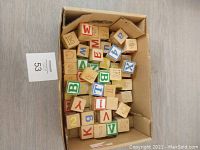 Top-down view of a box filled with vintage wooden toy blocks showing various letters, numbers, and symbols in multiple colors on cube shapes.