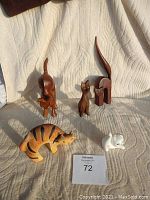 Photo showing five cat figurines on a white textured fabric background. Four wooden cats are variously posed with natural wood finish; one is a white ceramic cat.