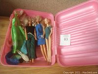 Pink plastic carrying case with Barbie dolls, assorted clothes and a hairbrush inside.