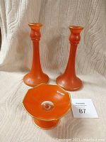 Orange glass candlesticks and pedestal dish arranged front-facing on cloth backdrop.