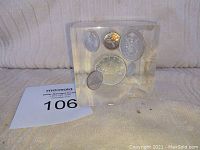 Lucite block with six embedded Canadian coins including a large silver dollar and smaller coins, with visible cracks and damage.