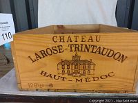 Front view of wooden wine box with burnt-in branding: Chateau Larose-Trintaudon, Haut-Medoc, illustration of chateau, holds 12 bottles
