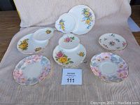 Top view of seven porcelain plates with varying floral patterns and shapes on a beige fabric background.