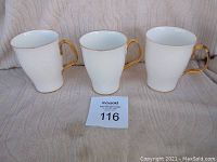 Three Royal Albert Val D'or mugs shown upright against a neutral background, displaying gold handles and white body.