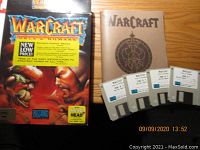 Full set including Warcraft game box, four floppy disks, and manual laid out on wooden surface.
