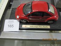 Red Maisto Volkswagen New Beetle model car on a black display base with nameplate.