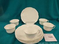 Five white porcelain lunch plates stacked with one saucer and cup placed on top in front of a solid teal background.