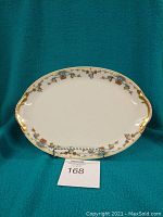 Front view of an oval Limoges platter with floral decoration and gold trim, displayed on a stand.