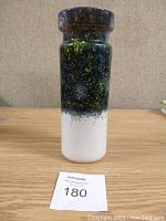 Full front view of tall cylindrical pottery vase with dark green and black speckled glaze over white base color.